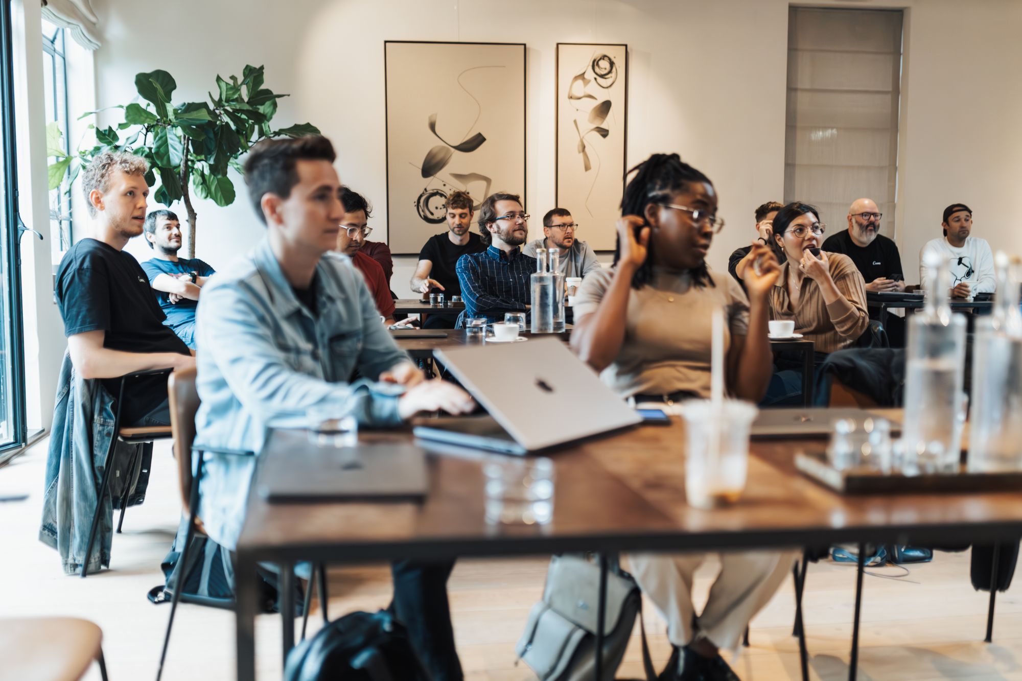Gruppe sitzt mit Laptops an Tischen und diskutiert in einem Workshop